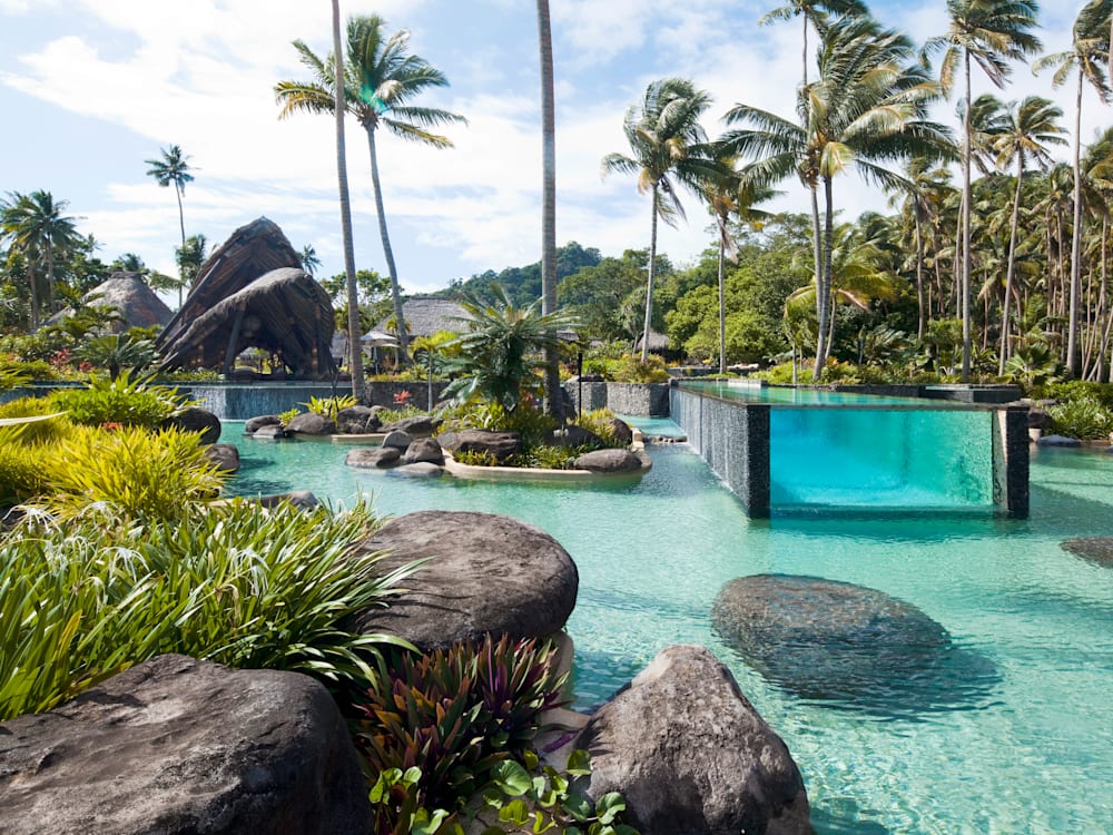 An infinity pool set within a larger swimming pool - surrounded by palm trees.