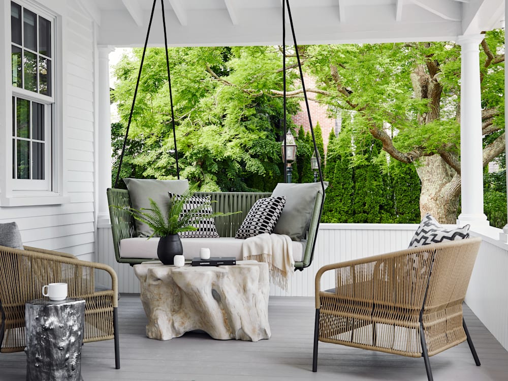 A swing chair with stylish furniture on a balcony surrounded by greenery