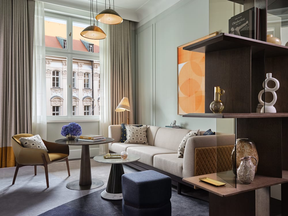 A sofa, tables and chairs next to a book shelf in the Deluxe Suite Lounge of the Rosewood Munich.