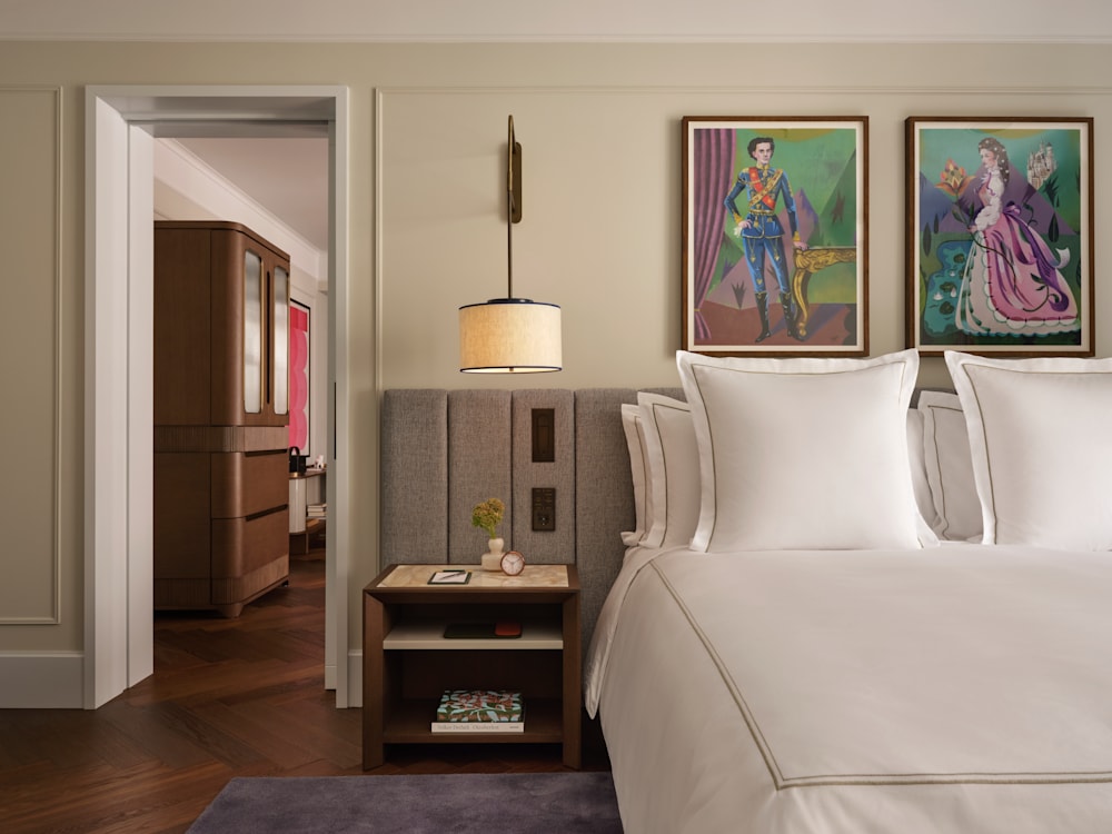 A white double bed in the Grand Premier Suite, beneath two colourful portraits.