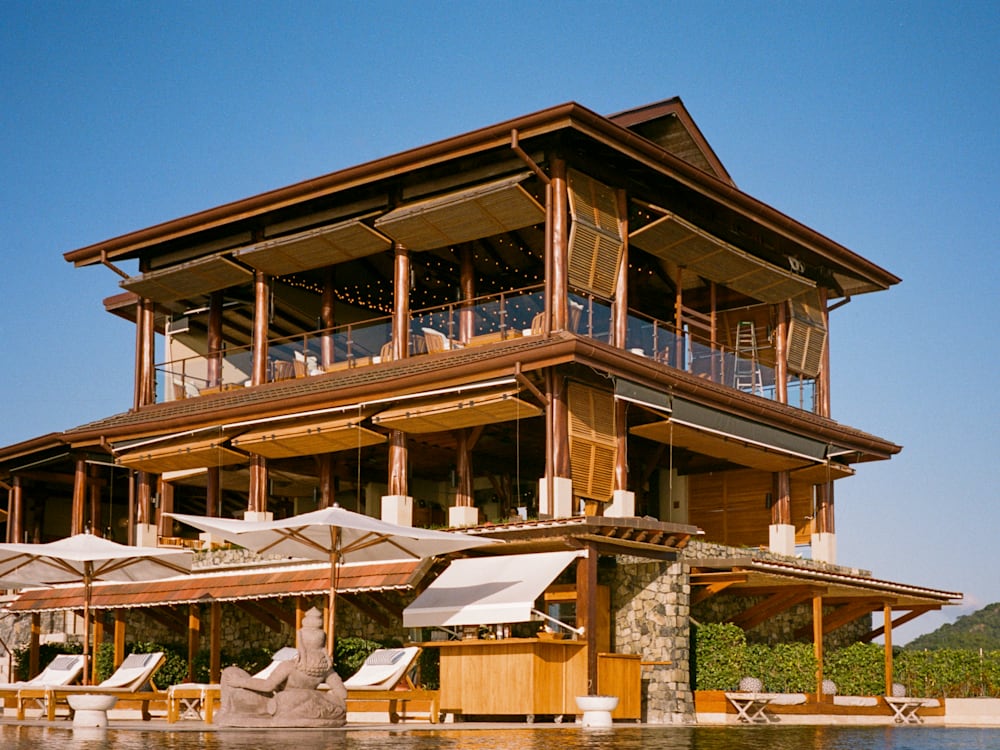 Wooden exterior of the Casa Chameleon Las Catalinas building. Parasols shade sun-loungers next to the pool.