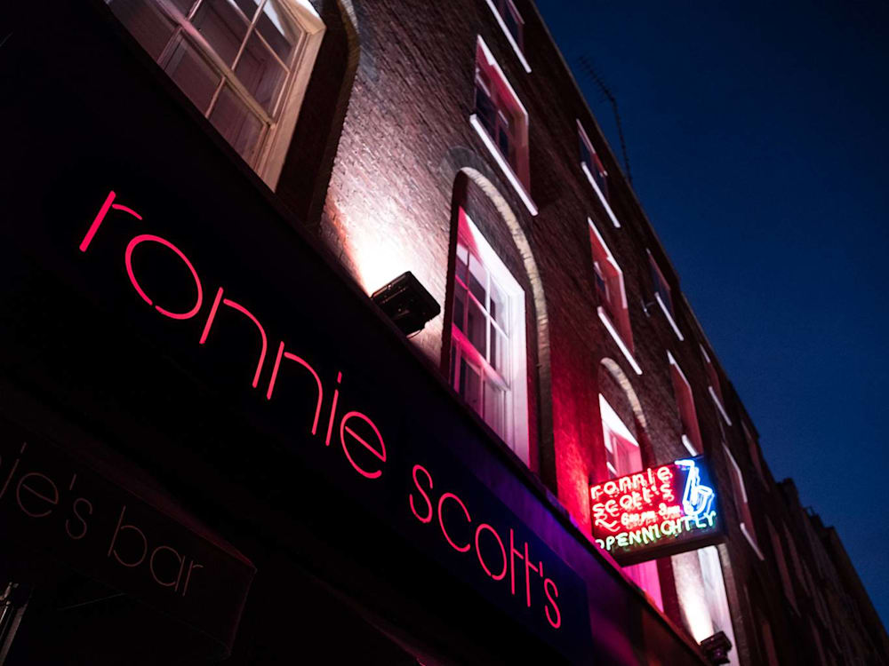 Exterior of Ronnie Scott's club at night, with two neon signs with the venue's name in red.
