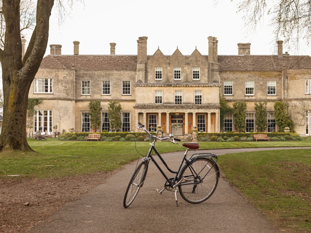 A bike is parked on a path outside the Lucknam Park hotel building, next to some grass