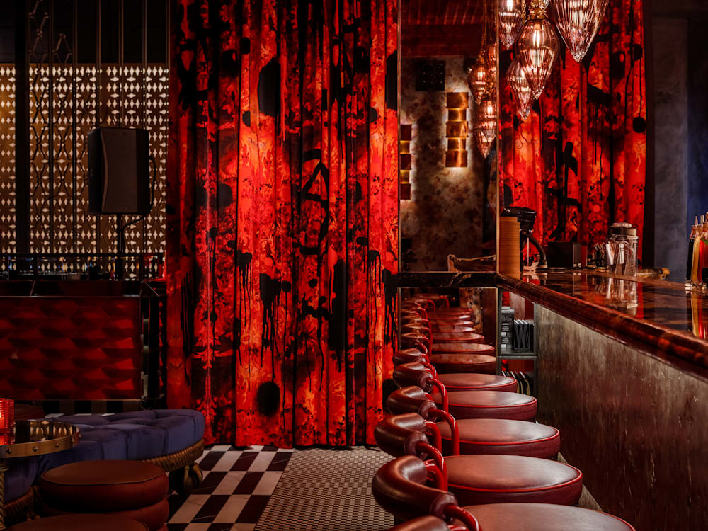 Red stools line a dimly lit bar, with red curtains hanging behind.