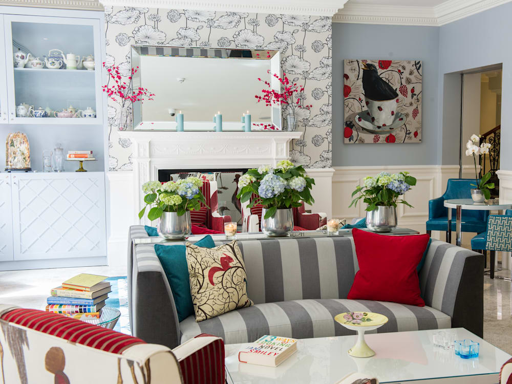 The reception room of the Ampersand Hotel.  The rooms are designed with maximalist interiors, including floral wallpaper, striped sofas, red cushions, blue walls, and flowers on the tables.