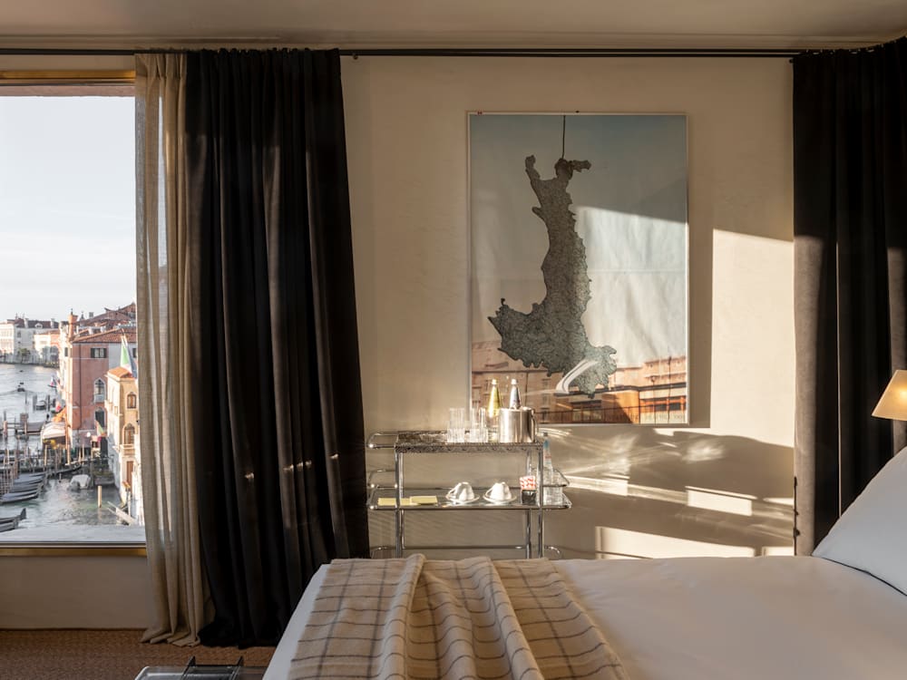 A bedroom in the Venice Venice hotel. A painting is hung next to the bed, with a window to the left over the canals.