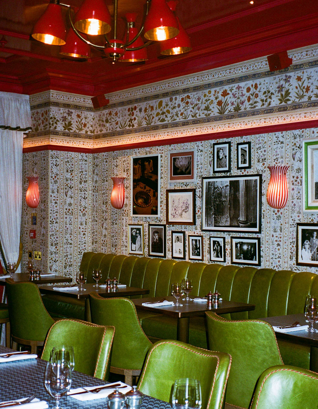 A flash film photo of a restaurant with green chairs and a red ceiling. Art hangs on the wallpaper walls.